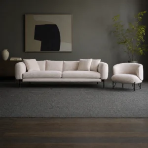 Sofagarnitur in Creme mit rundem Sessel daneben, davor ein dunkelgrauer Teppich vor einer dunklen Wand