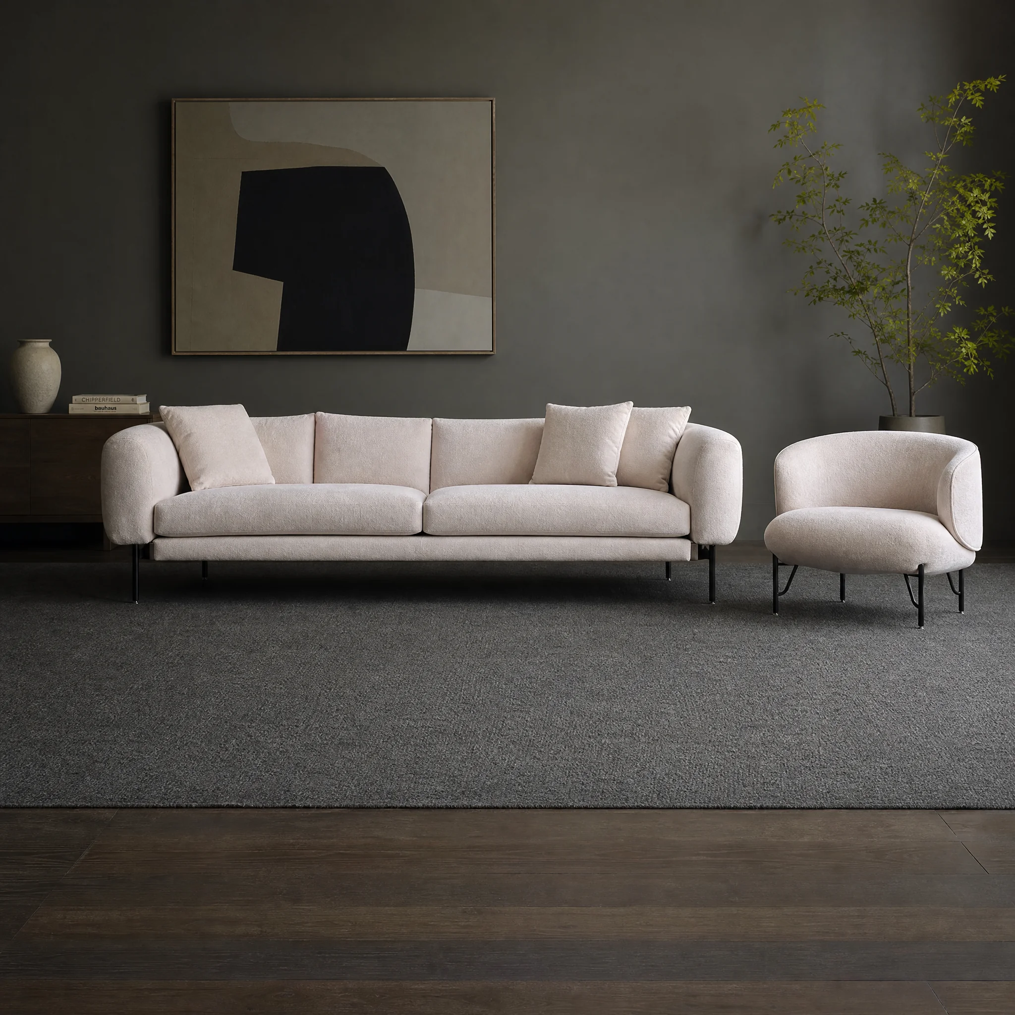 Sofagarnitur in Creme mit rundem Sessel daneben, davor ein dunkelgrauer Teppich vor einer dunklen Wand